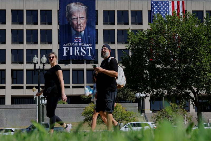 Pedestrians pass a large banner featuring U.S. President Donald Trump hanging on the Department of Labor building in Washington, D.C., U.S., in Washington, D.C., U.S., August 26, 2025.   REUTERS/Brian Snyder