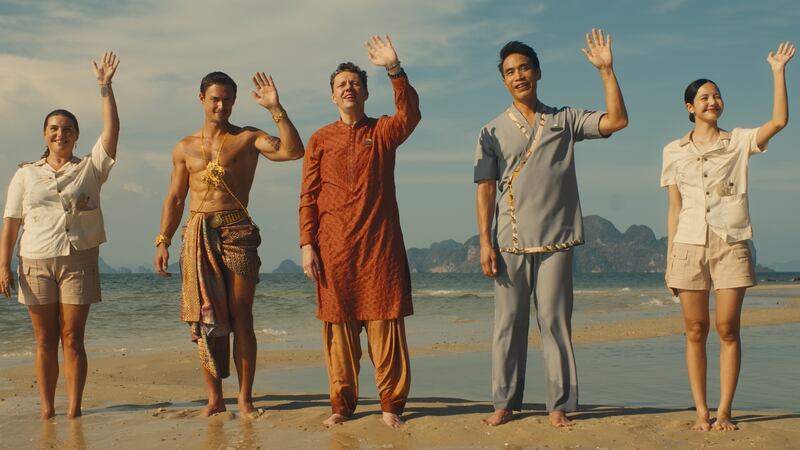 Five people stand on a beach while waving.