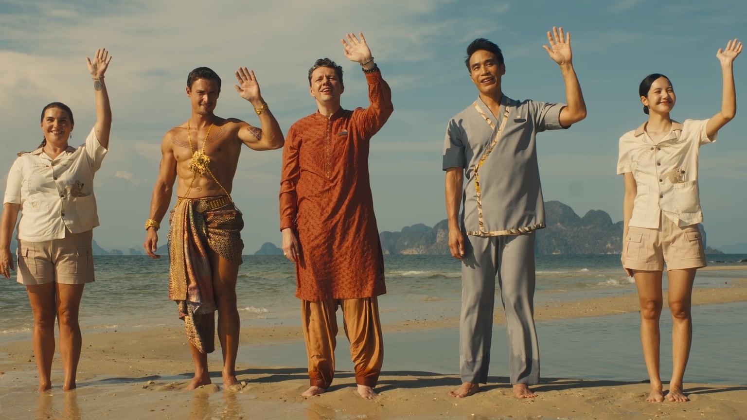 Five people stand on a beach while waving.