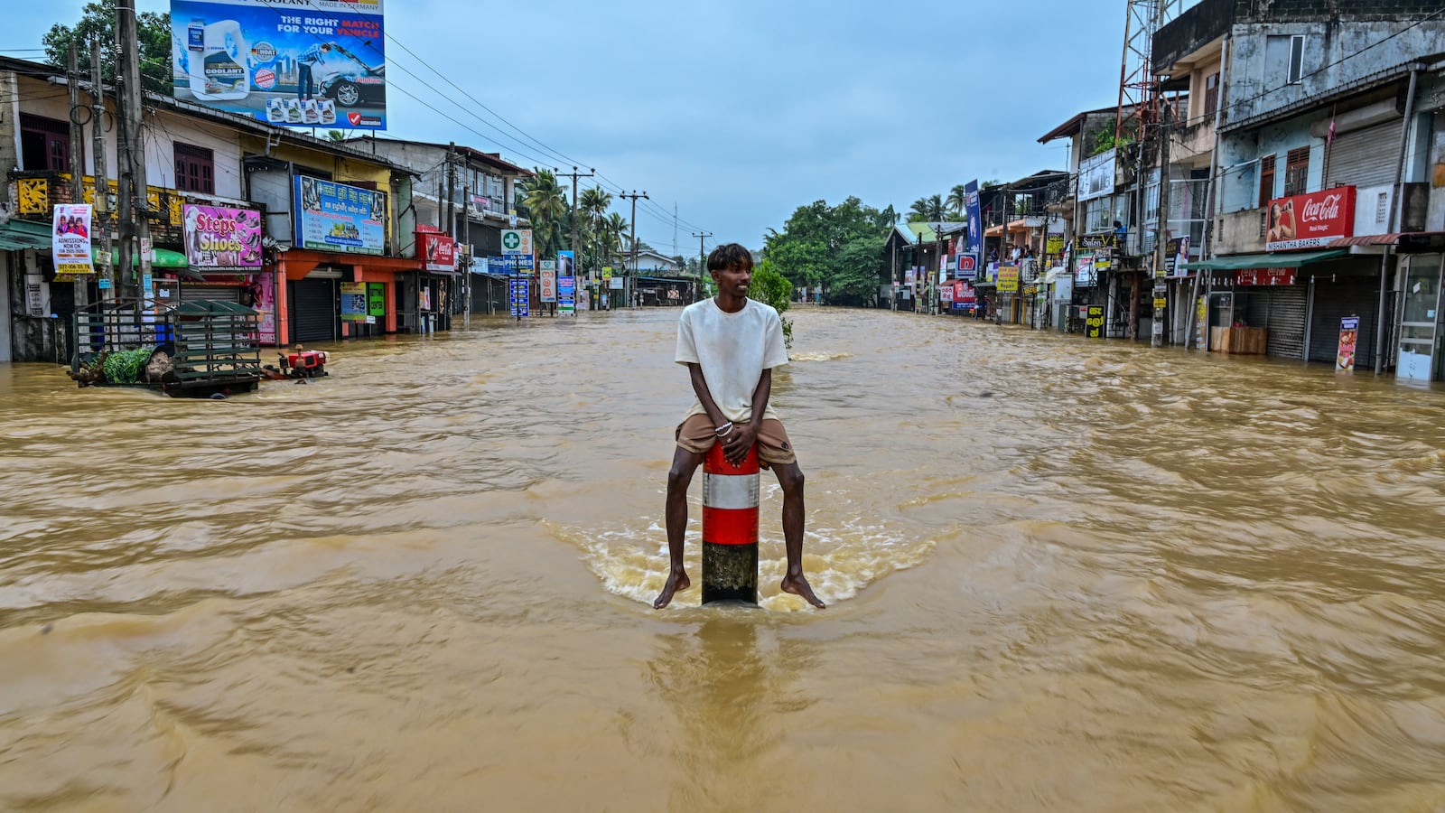 TOPSHOT - A man sits on a divider in the middle of a flooded road after heavy rainfall in Kaduwela on the outskirts of Colombo on November 29, 2025. Sri Lanka made an appeal for international assistance on November 29 as the death toll from heavy rains and floods triggered by Cyclone Ditwah rose to 123, with another 130 reported missing. (Photo by Ishara S. KODIKARA / AFP via Getty Images)