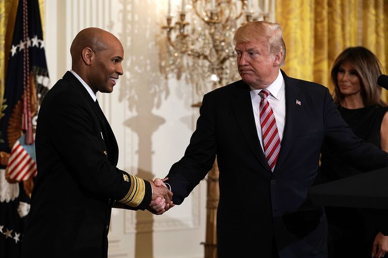 President Donald Trump shakes hands with Surgeon General Jerome Adams as Melania Trump in 2018.