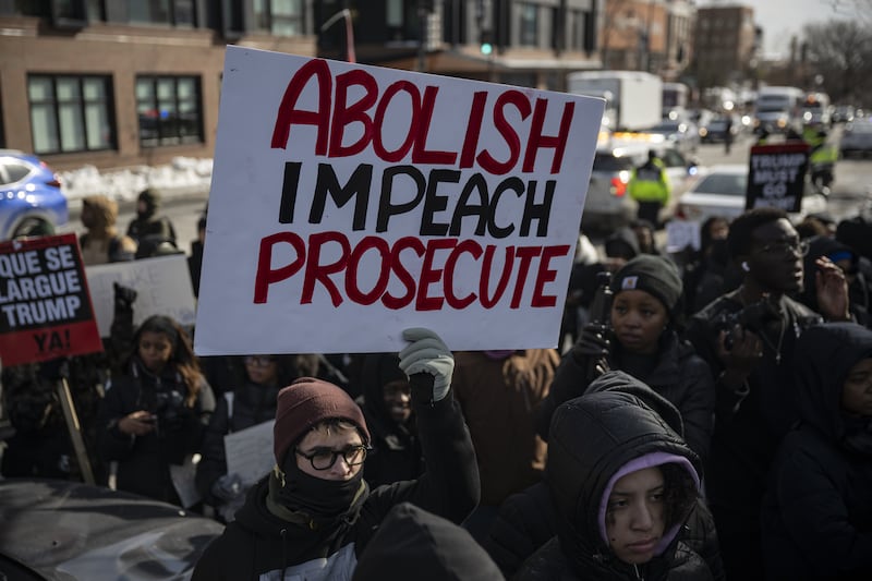 A masked man holds a sign in a crowd that says "ABOLISH, IMPEACH, PROSECUTE"