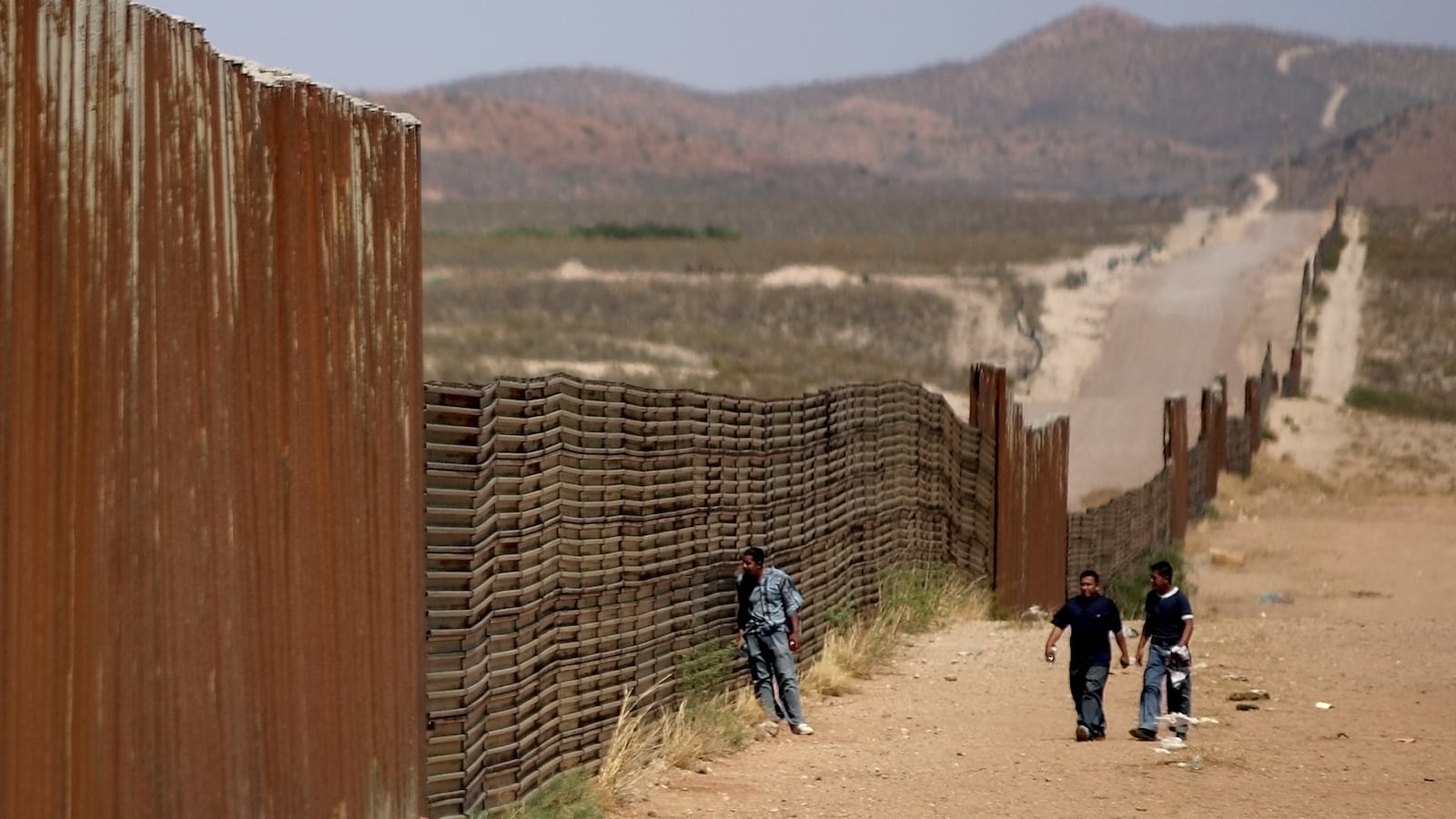 Mexican men walk along the border wall that separates Agua Prieta, Sonora, Mexico from Douglas, Arizona, U.S., May 23, 2006.