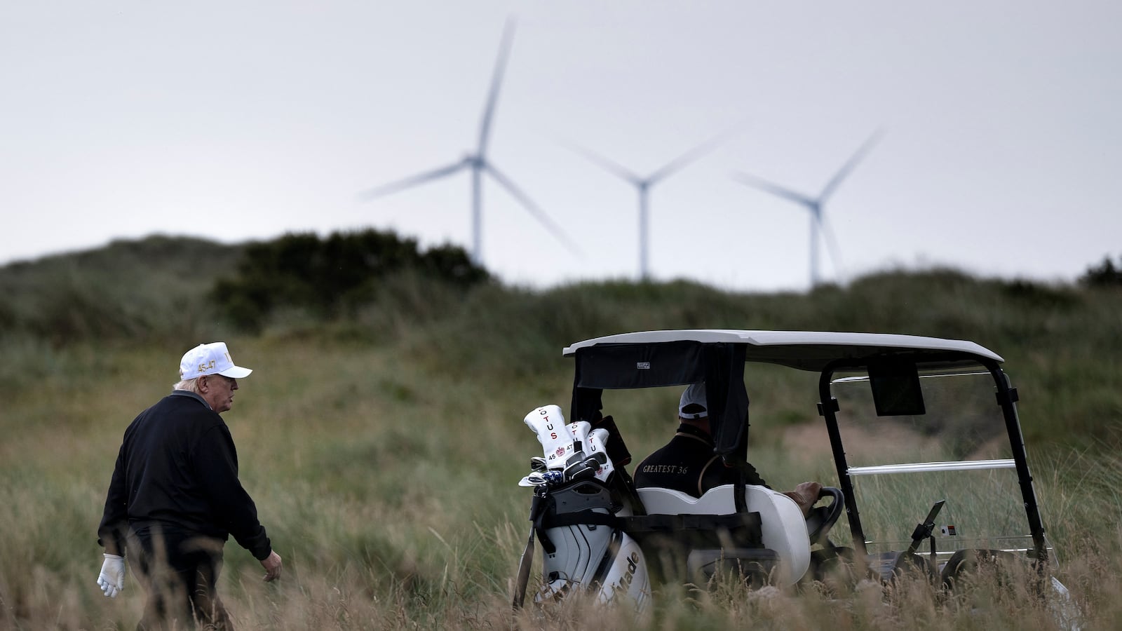 US President Donald Trump (L), backdropped by Turbines at the European Offshore Wind Deployment Centre, also known as the Aberdeen Bay Wind Farm, walks on the first fairway after playing off the first tee to officially open the Trump International Golf Links course in Balmedie, Aberdeenshire, north east Scotland on July 29, 2025. (Photo by Brendan Smialowski / AFP) (Photo by BRENDAN SMIALOWSKI/AFP via Getty Images)
