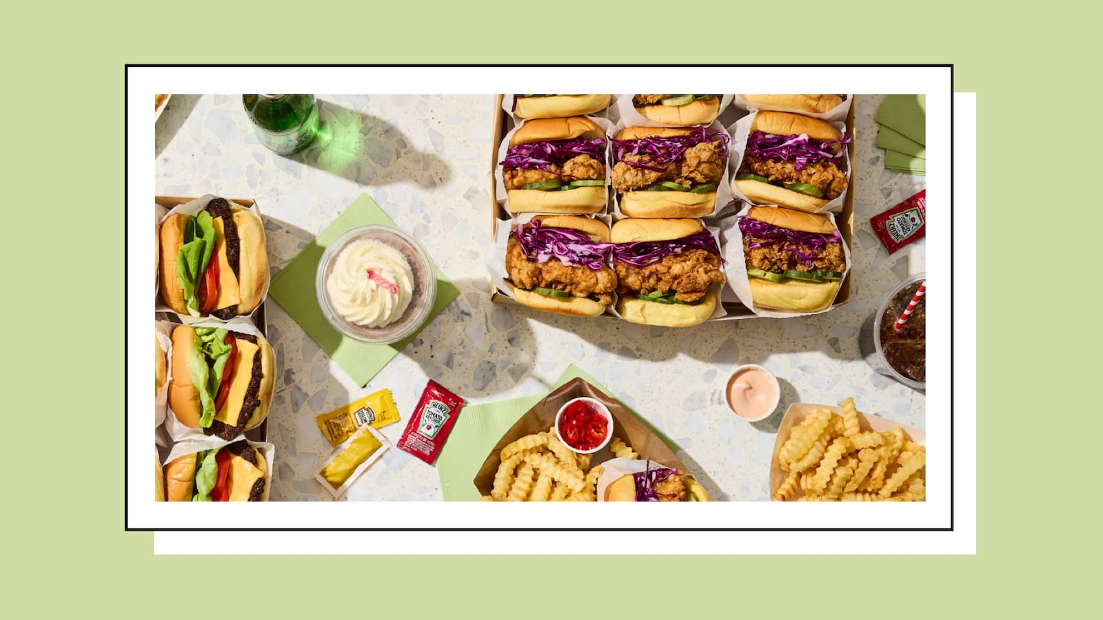 A catered office lunch order from ezCater featuring fried chicken sandwiches, cheeseburgers, crinkle-cut fries, and dipping sauces displayed in an overhead flat-lay.