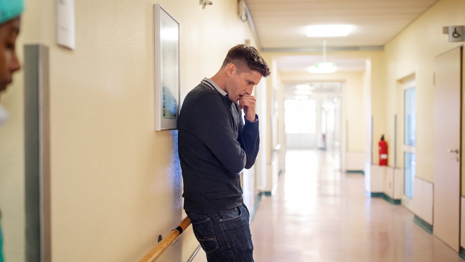 Young man standing in hospital corridor looking worried. Man filling nervous standing at hospital corridor waiting while a doctor in foreground.