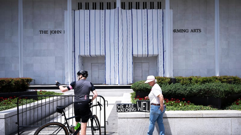 People stand in front of a tarp covering signage on the facade of the Kennedy Center in Washington, DC, on June 15, 2026, after a judge ordered the removal of US President Donald Trump's name from the building.