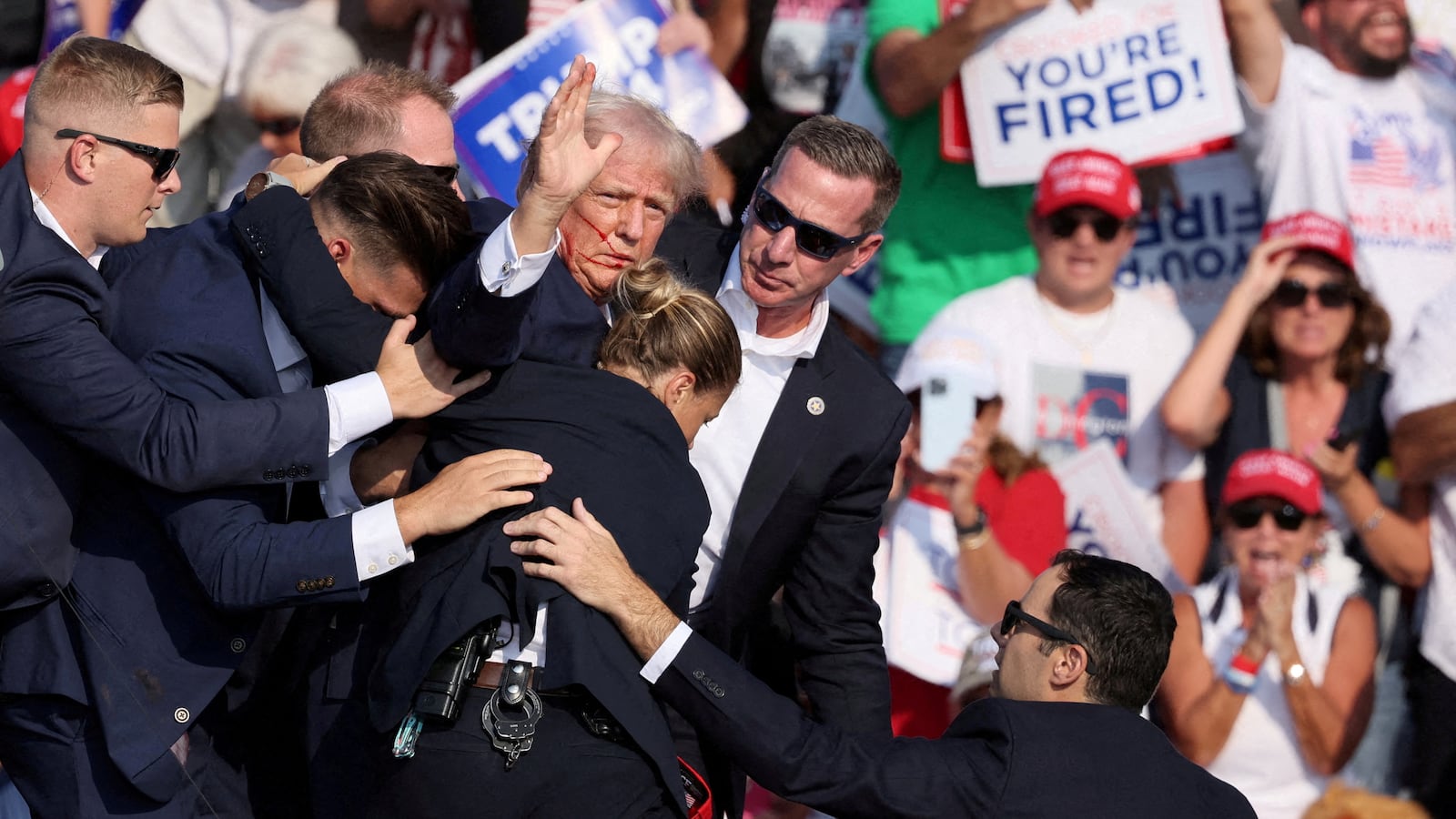 Donald Trump holds up a hand while he's rushed off stage by the Secret Service.