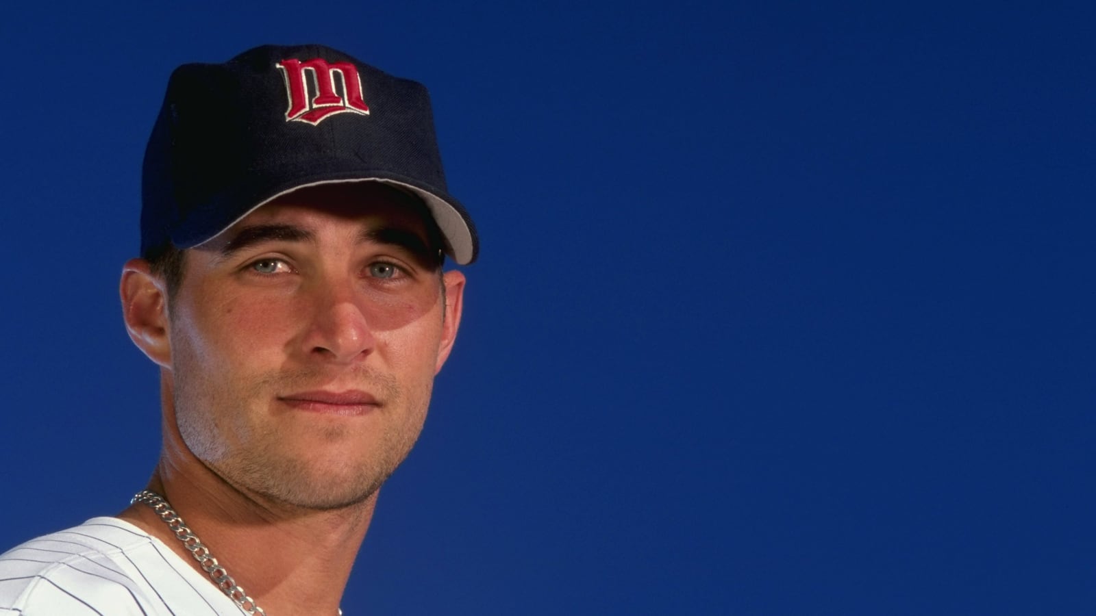 Baseball player wears a cap while posing for the camera in front of a blue background.