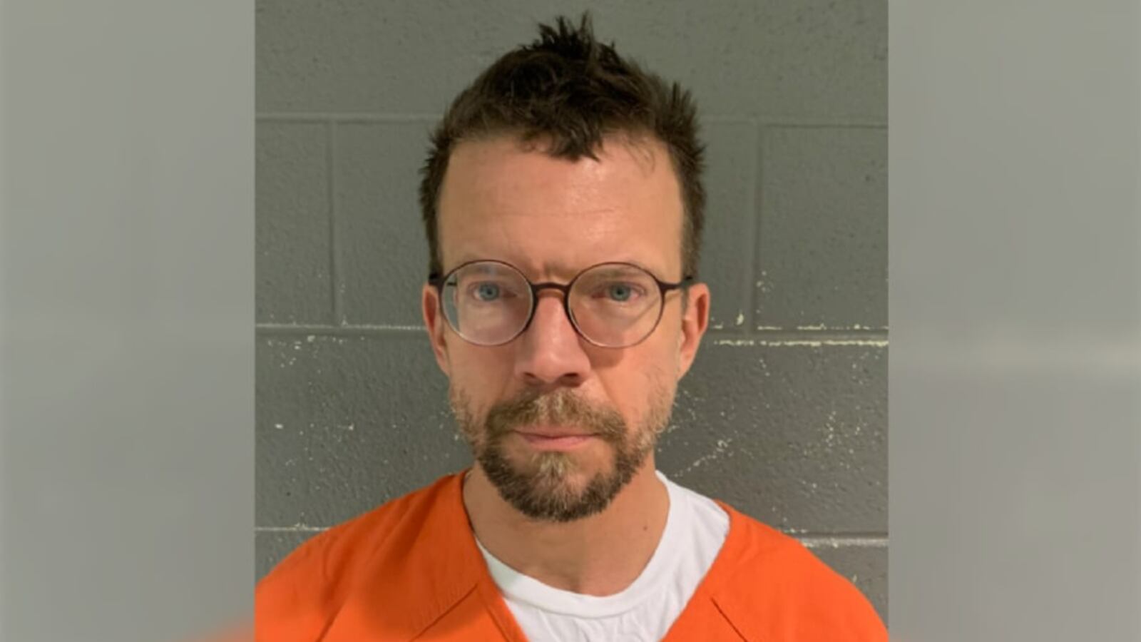 A mugshot of Patrick Wojhan, who is wearing orange in front of a grey background as he stares forward.