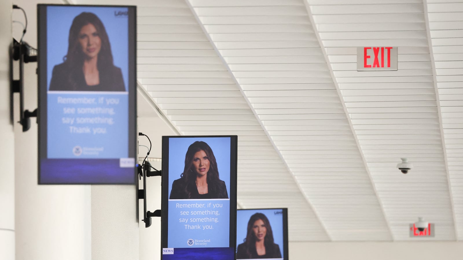 A video featuring former Department of Homeland Security (DHS) Secretary Kristi Noem is displayed above a Transportation Security Administration (TSA) checkpoint