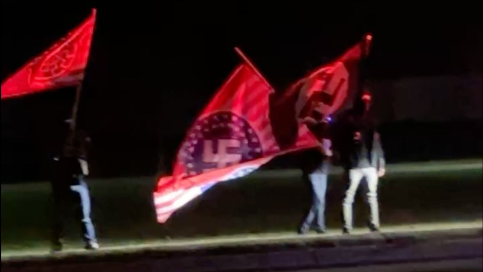 A video still shows masked protestors waving flags with Nazi insignia outside American Legion Post 141 in Howell, MI.