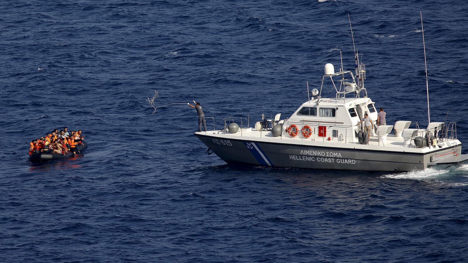 A Greek Coast Guard officer throws a towing rope at a drifting dinghy overcrowded with refugees and migrants off the Greek island of Lesbos, after the dinghy crossed a part of the Aegean Sea from the Turkish coast, Sept. 21, 2015.