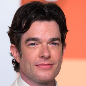 John Mulaney next to an image of the crashed car with a bullet hole in the window after Jonathan Ross shot and killed Renee Nicole Good in Minneapolis, Minnesota