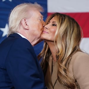 President Donald Trump kisses the First Lady Melania Trump on the cheek in from of a giant USA flag