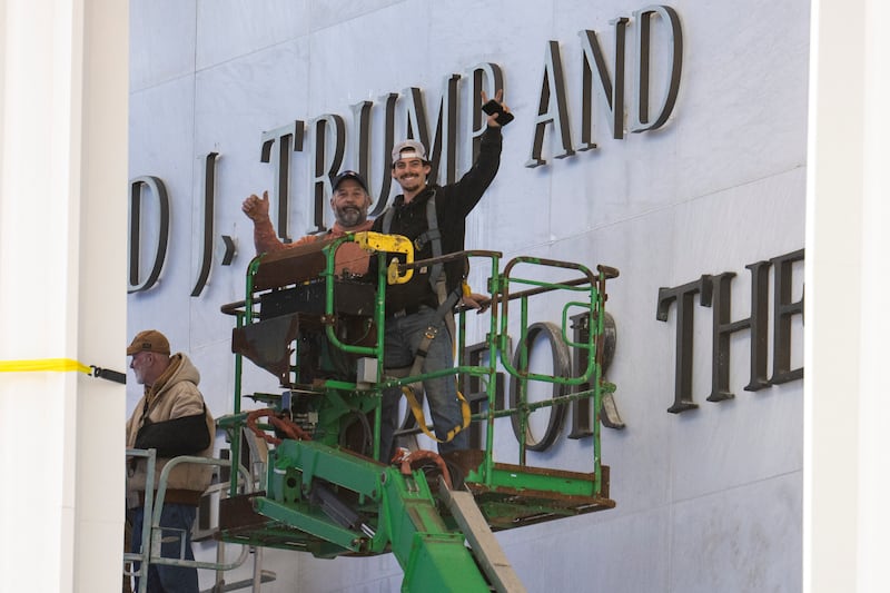 Workers react to the media as they come down off a scissor lift after updating signage outside the The John F. Kennedy Memorial Center for the Performing Arts