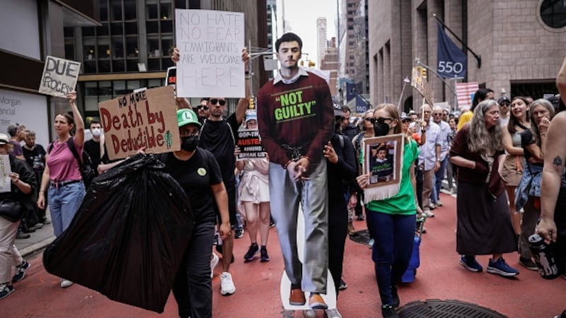 A woman carries a poster with the image of Luigi Mangione as people hold up signs, during a rally titled "Protect Migrants, Protect the Planet," in New York City
