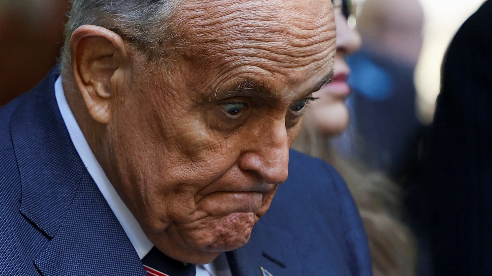 Rudy Giuliani grimaces while staring down at an outdoor event.