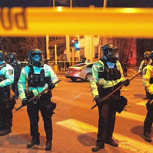 Law enforcement officers guard the perimeter of the scene as residents protest a federal agent-involved shooting
