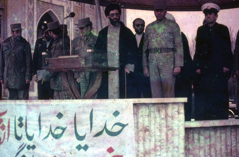 View of Iranian President Ali Khamenei surrounded by soldiers and clerics speaking on stage at a lectern in Iran, March, 1983. The banner attached to the dais is written in Farsi and is obstructed. The visible portion translates to: "God, God until...".