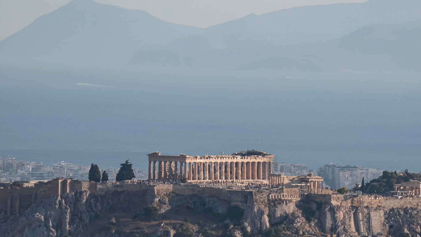 Panoramic view of the Parthenon and the Acropolis of Athens seen from a hill with the city and the sea in the background. The ancient temple and the surrounding buildings like Temple of Athena Nike, Propylaea and Erechtheion are of great architectural and historical significance, enlisted as a UNESCO World Heritage Site. Acropolis is flocked with tourists and visitors from all over the world after a heatwave which resulted the monument to remain closed during the early evening hours with the high temperature. Athens, Greece on July 2024. (Photo by Nicolas Economou/NurPhoto via Getty Images)
