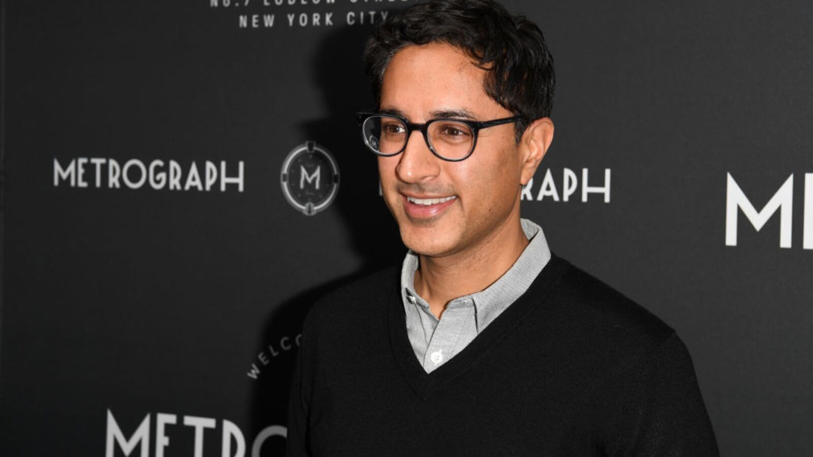 Maulik Pancholy poses in front of an advertising board.