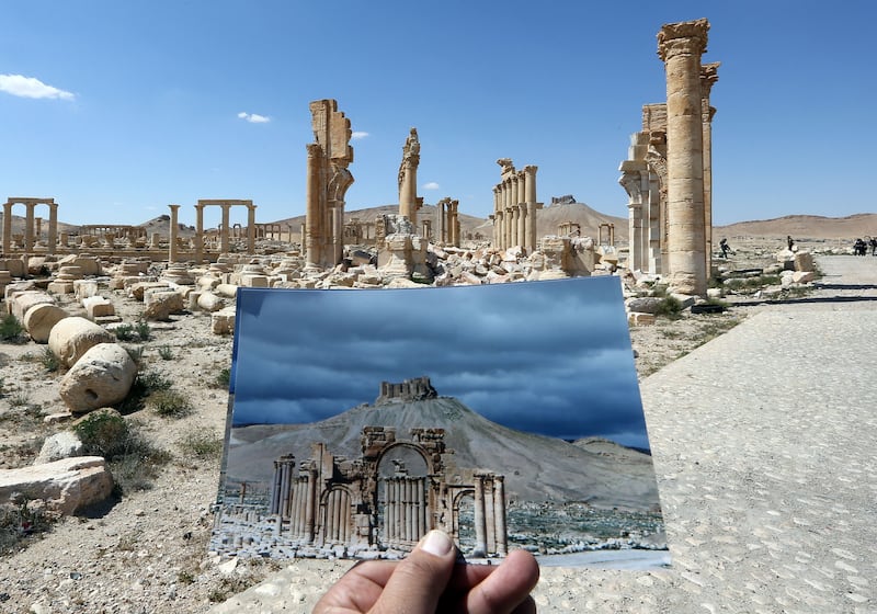 A general view taken on March 31, 2016 shows a photographer holding his picture of the Arc du Triomphe (Triumph's Arch) taken on March 14, 2014 in front of the remains of the historic monument after it was destroyed by Islamic State (IS) group jihadists in October 2015