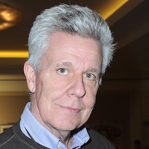 A grey-haired man holds an action figure of a man in a gimp costume.