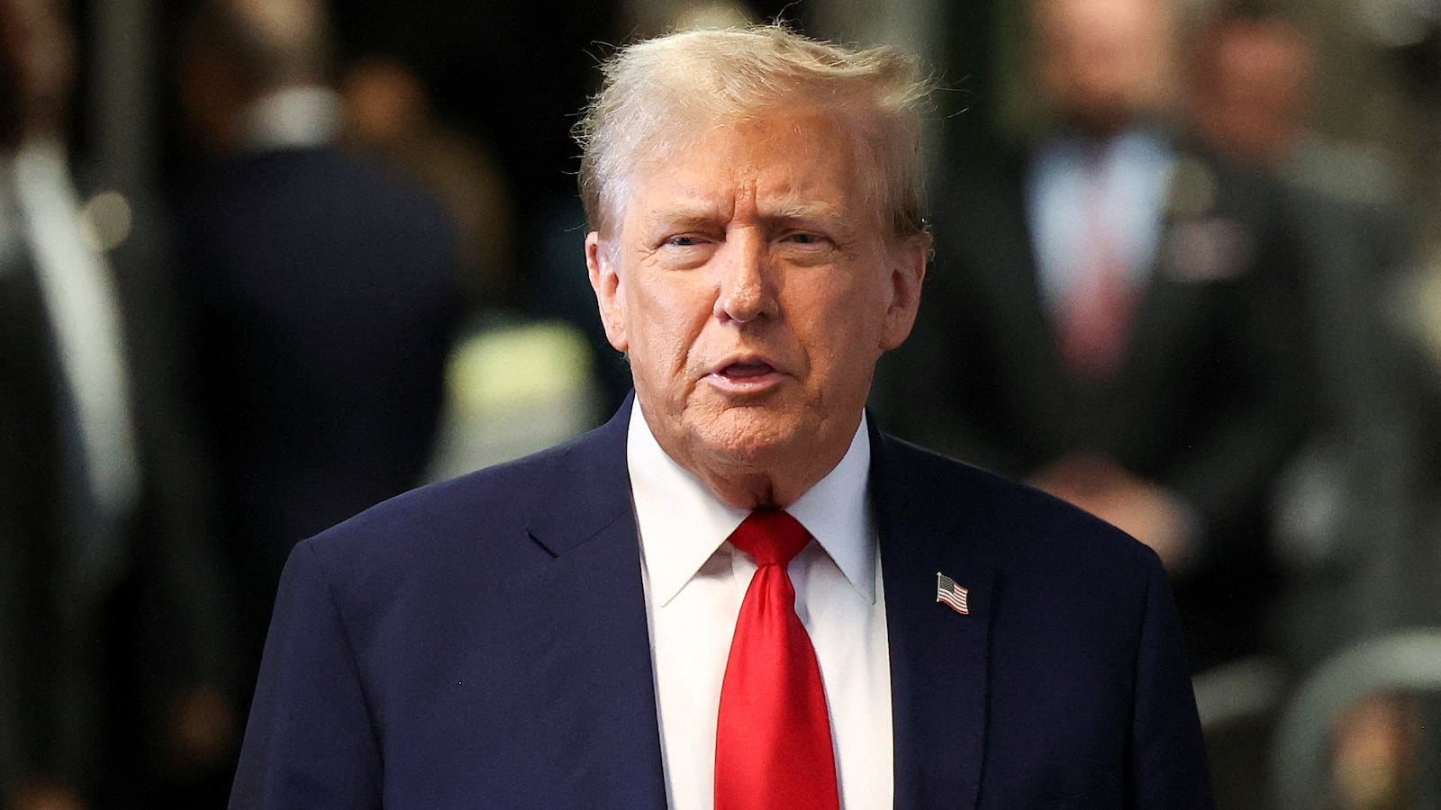 Donald Trump speaks while leaving court in a suit and tie.