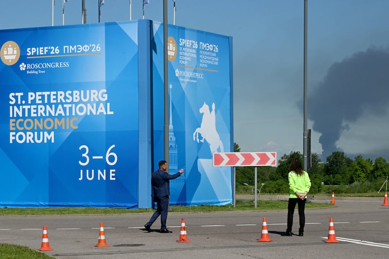 TOPSHOT - People are seen in front of banners with branding for the St. Petersburg International Economic Forum (SPIEF) as black smoke rises in distance in Saint Petersburg on June 3, 2026. Ukrainian drones hit energy and military sites in Saint Petersburg early Wednesday morning as officials gathered for a flagship economic forum in the city, Russian and Ukrainian authorities said. Saint Petersburg Governor Alexander Beglov, said "several" infrastructure facilities were damaged, but no one was killed in the attack. (Photo by AFP via Getty Images)