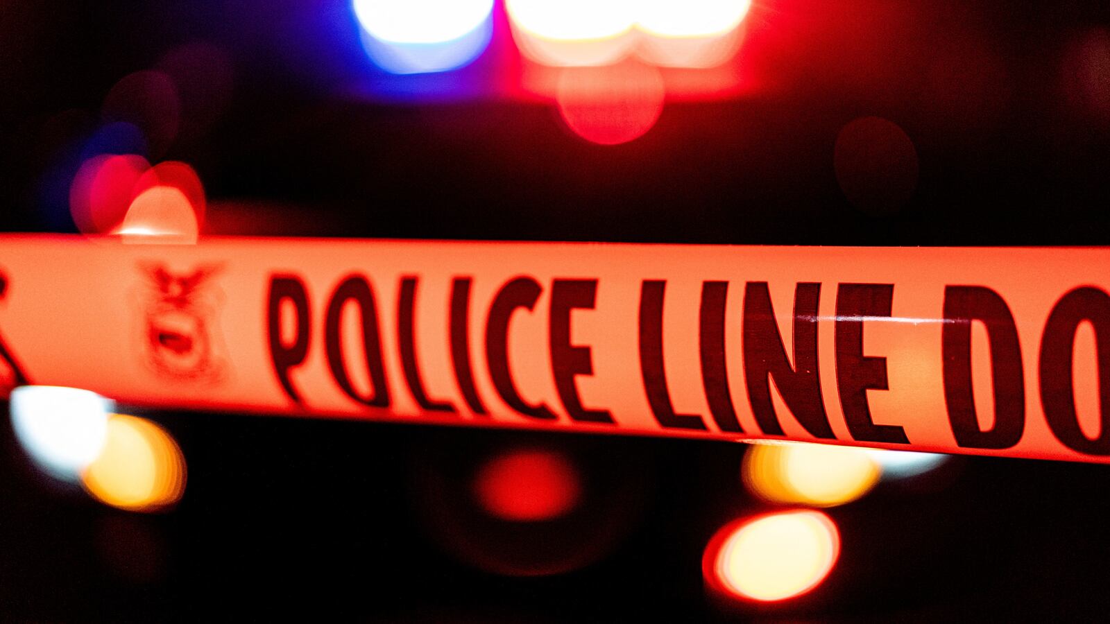 Police tape in front of flashing police lights.
