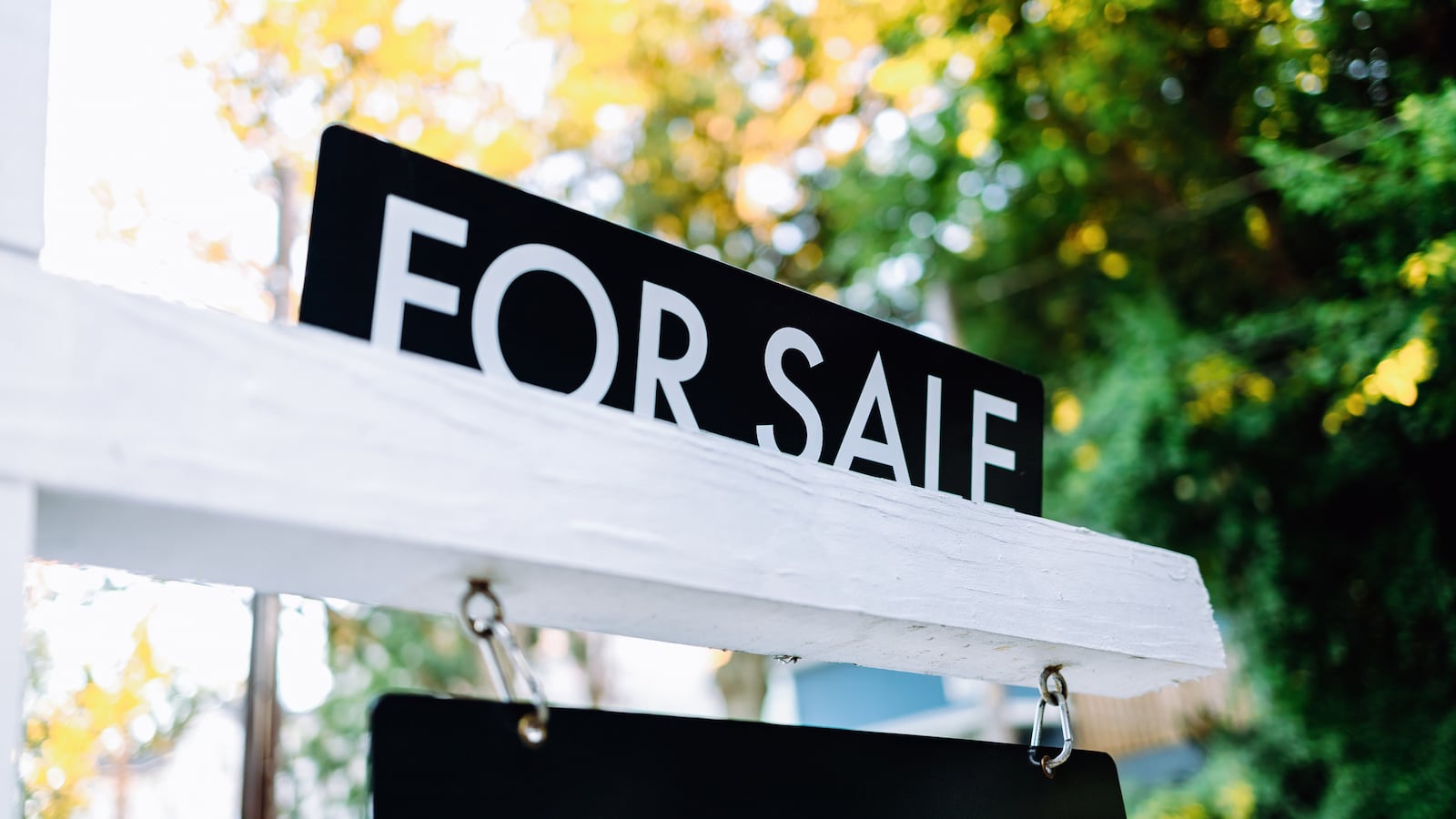 Close-up of for sale rider on real estate sign post in front yard of house.