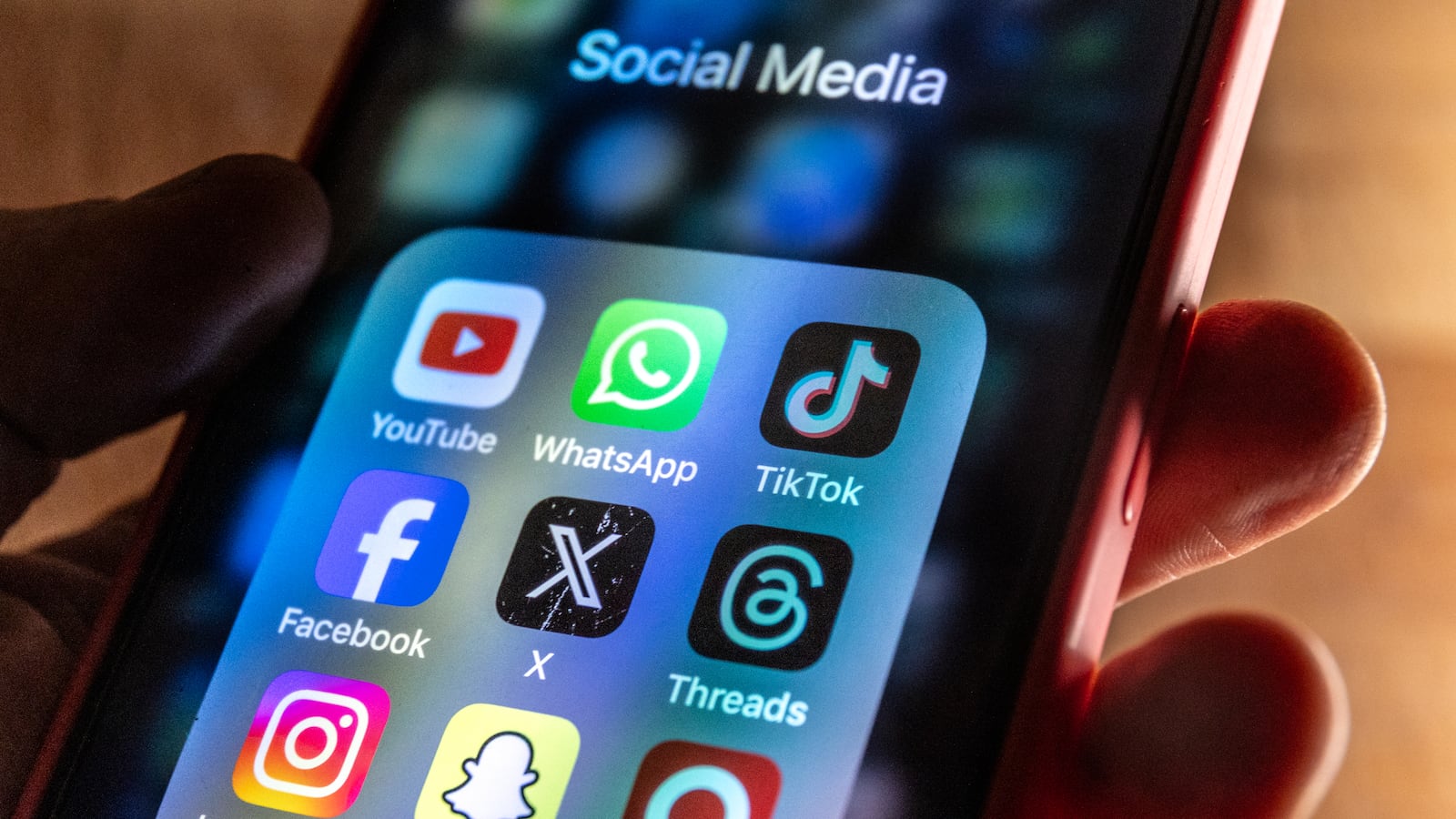 In this photo illustration, A man holds a smartphone iPhone screen showing various social media apps including YouTube, TikTok, Facebook, Threads, Instagram and X on March 13, 2024 in Bath, England.