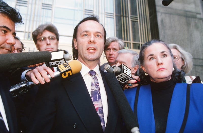 A man speaks to the press outside of a court building with a gaggle of people standing behind him.