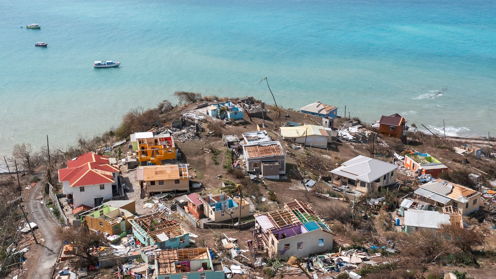 A drone-eye view of shattered houses on a peninsula, behind it is crystal-clear water