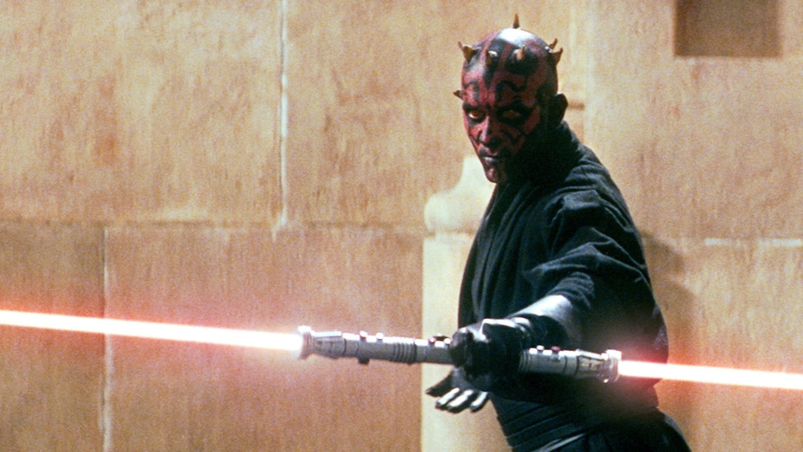 A man with a red and black face holds a lightsaber.