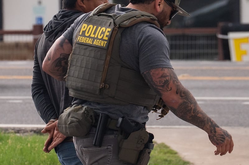 A man is led into a vehicle in handcuffs as an ICE agent makes an arrest following a traffic stop