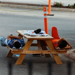 A photo of migrants laying on a bench outside the City of San Antonio Migrant Resource Center.
