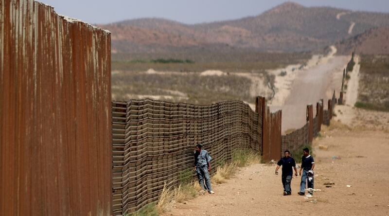Mexican men walk along the border wall that separates Agua Prieta, Sonora, Mexico from Douglas, Arizona, U.S., May 23, 2006. Immigrants say they will keep crossing the border despite U.S. plans to build more fences and send the National Guard to keep them out.