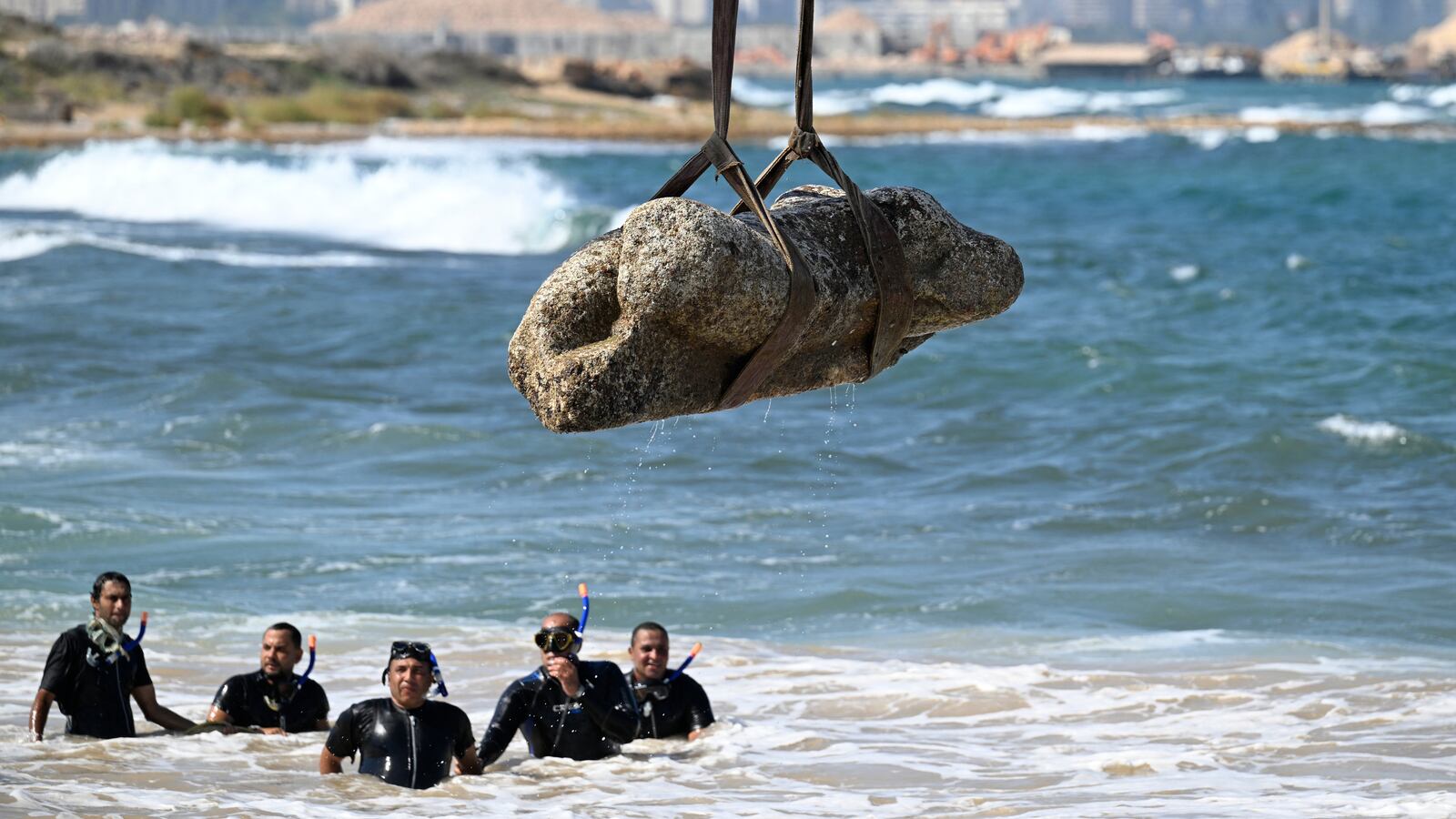 TOPSHOT - Divers watch as a crane pulls an artifact from the waters at Abu Qir bay in Alexandria on August 21, 2025, as part of an event organized by the Ministry of Tourism and Antiquities to recover sunken antiquities.