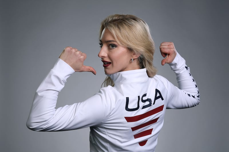 A blonde woman faces away from the camera pointing to the 'USA' logo on the back of her jacket.