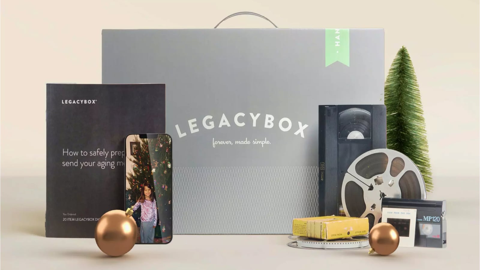Legacybox kit with VHS tapes, film reels, photos, and smartphone showing digitized family memories