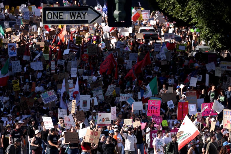 A crowd of protestors march under a sign that says "ONE WAY"