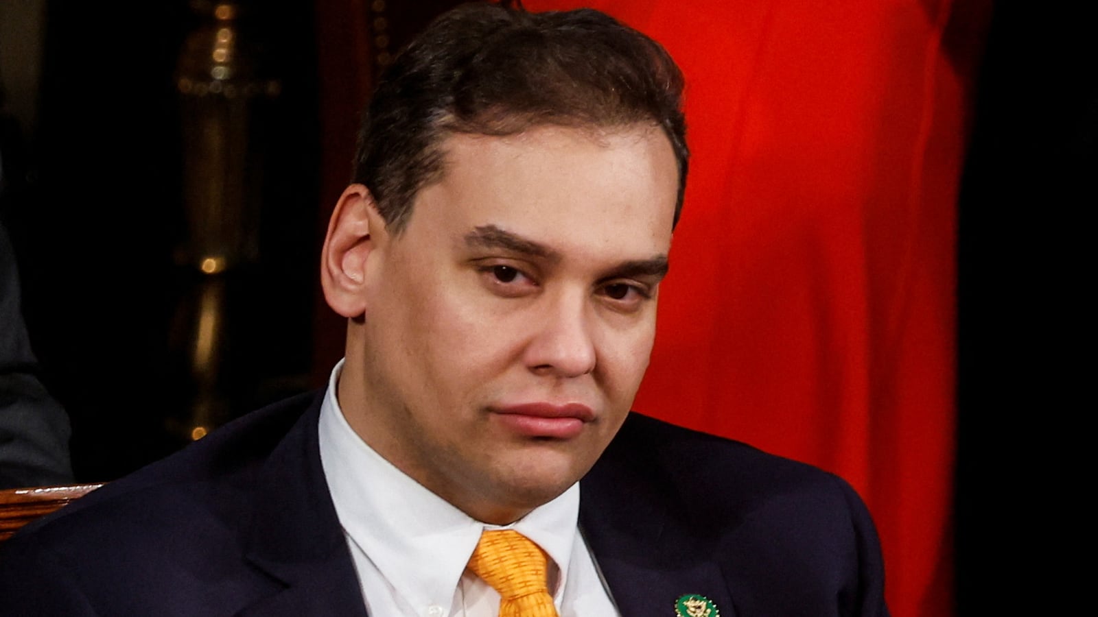 George Santos sits with a miserable look on his face.