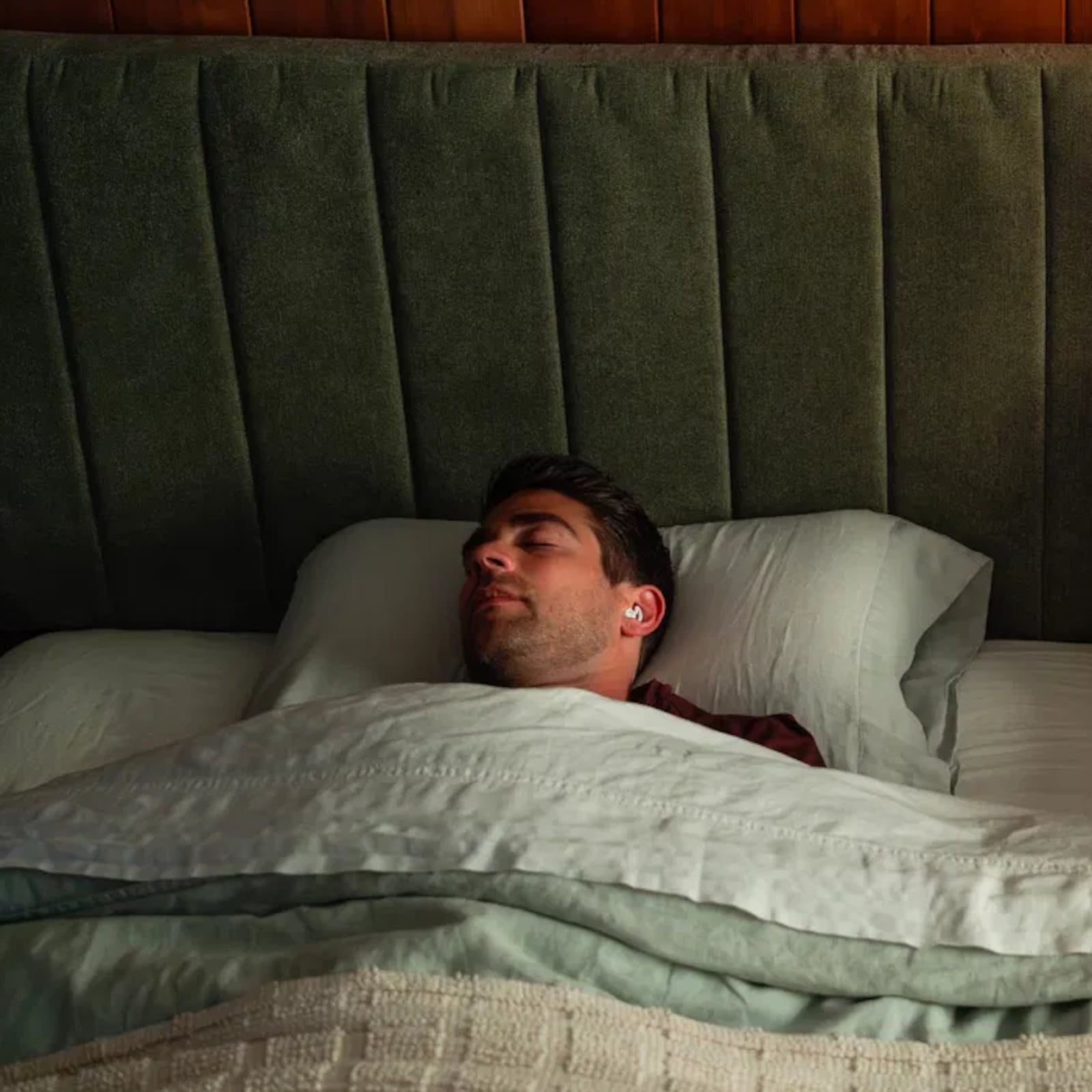 A man wearing Ozlo Sleepbuds asleep in a bed next to a woman reading a book