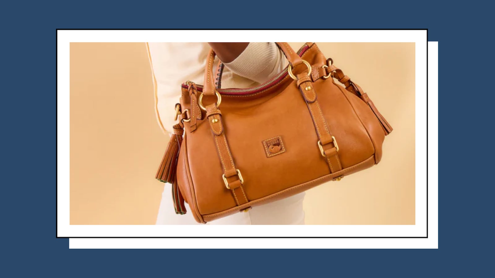 Woman holding a tan Dooney & Bourke Florentine satchel, showcasing the soft leather, tassel details, and gold hardware.