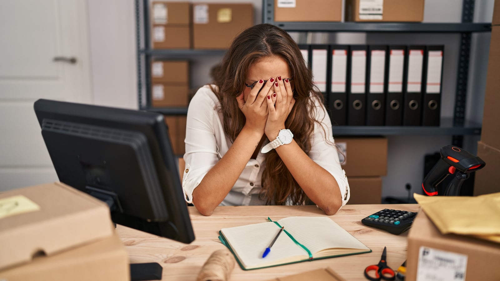 Young hispanic woman working at small business ecommerce with sad expression covering face with hands while crying.