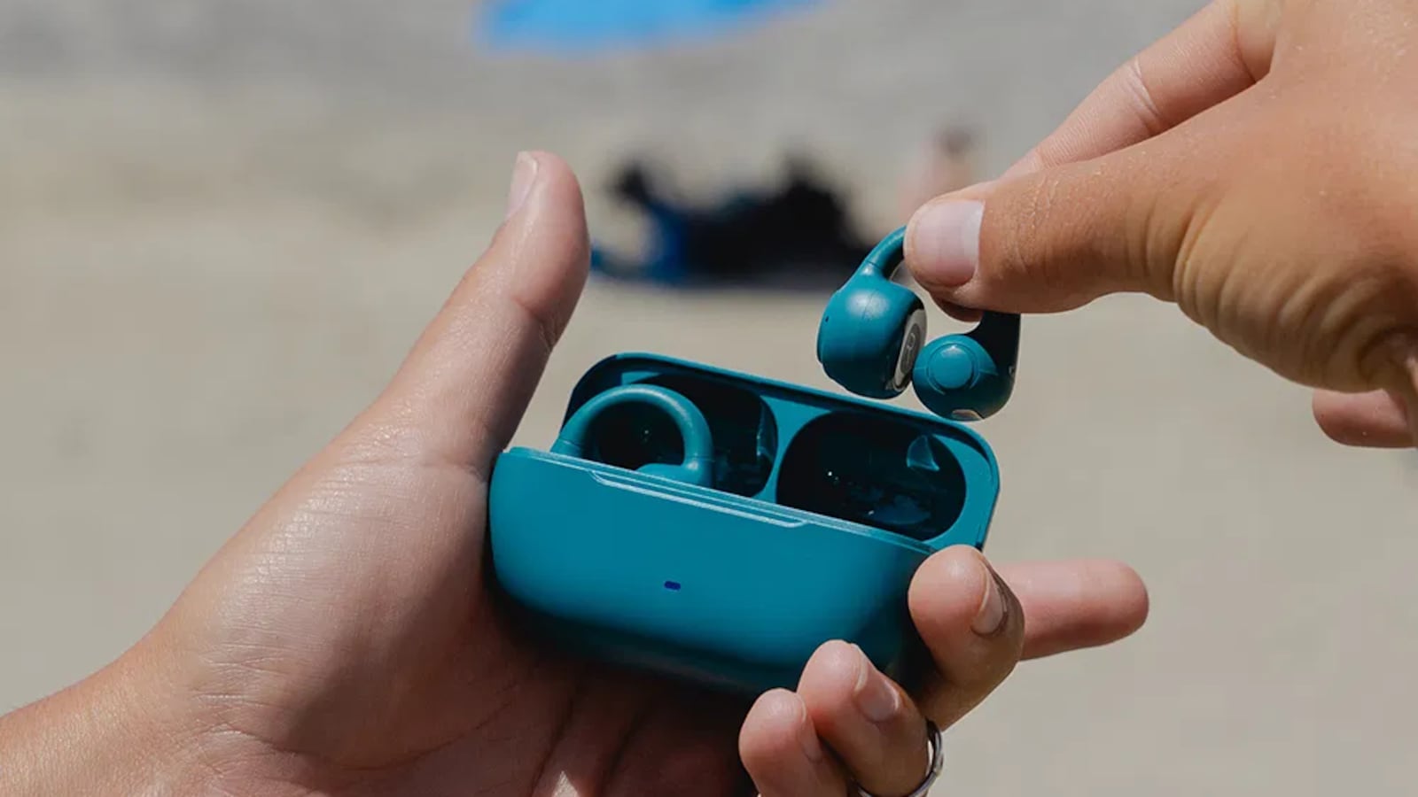 A person holding a pair of teal JLab wireless earbuds open in their hand.