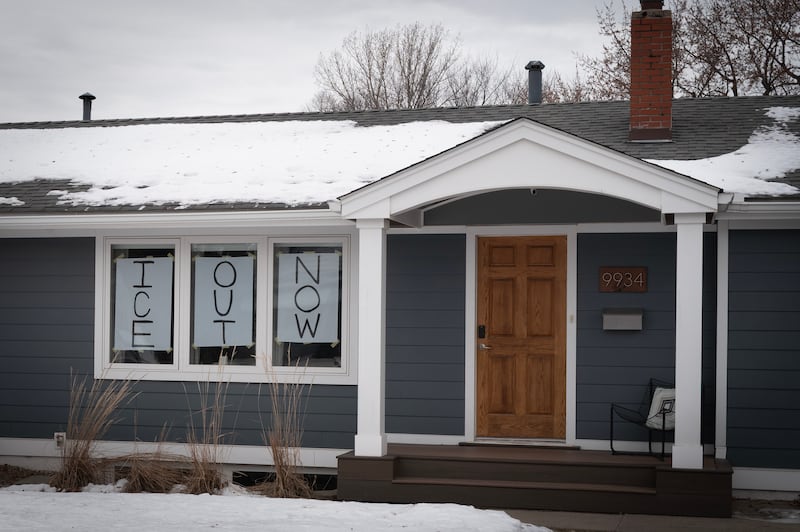 Handwritten signs reading "ICE Out Now" are displayed in the front windows of a home
