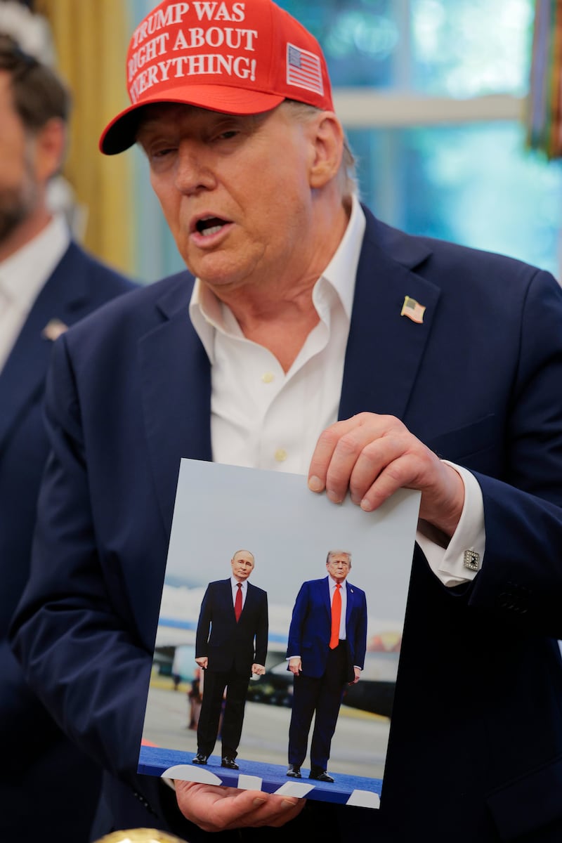 Trump in a red "Trump Was Right About Everything!" hat holds up a picture of himself with Vladimir Putin